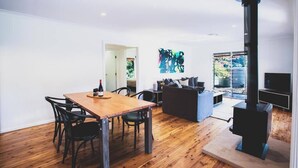 A modern living room with a wooden dining table, black chairs, a sofa, a fireplace, and a TV.