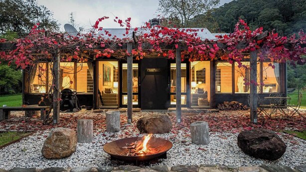 A modern cabin with a fire pit, wooden benches, and a garden with red foliage. - Jacaranda at Barranca - Luxury Villa (Kangaroo Valley)