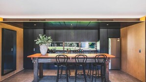 A modern kitchen with a wooden table and chairs, a large plant, and a view of the outdoors. - Jacaranda at Barranca - Luxury Villa (Kangaroo Valley)