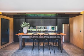 Una cucina moderna con un tavolo e sedie in legno, una pianta grande e vista sull'esterno.