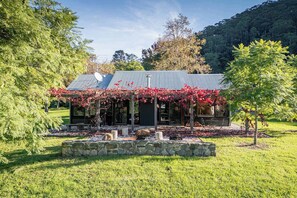 A modern house with a metal roof, surrounded by a stone wall and lush greenery.
