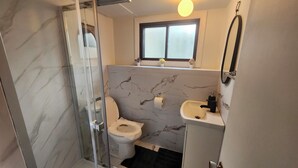 A bathroom with a glass shower enclosure, a toilet, a sink, and a window above the sink.