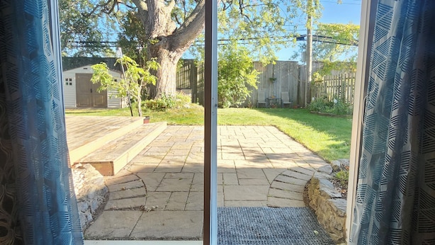 A sliding glass door leading to a backyard with a tree, a wooden deck, and a stone pathway.