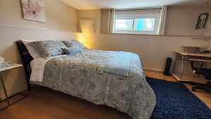 A bedroom with a bed, a desk, a chair, a window, and a wall-mounted plant.