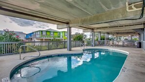 A swimming pool with a concrete deck, surrounded by a metal railing and a covered area with chairs and tables.