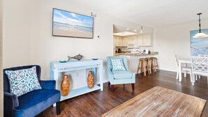 A living room with a blue sofa, a light blue armchair, a wooden coffee table, and a dining area with white chairs and a table.