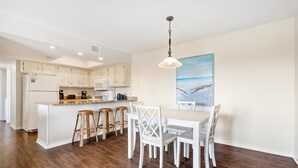 A modern kitchen with white cabinets, a central island, and a dining area with white chairs and stools.