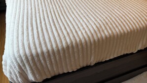 Una cama con cabecera oscura, almohadas blancas y colcha blanca con textura.