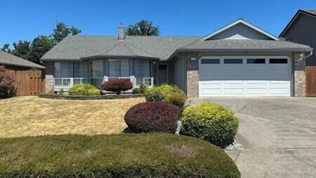 A single-story house with a garage, a well-maintained lawn, and a small garden with shrubs and a tree. - A three bedroom house with 2 bathrooms (Gresham)