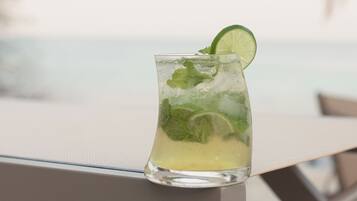 Un verre d’une boisson à base de citron vert, garni de feuilles de menthe, posé sur une table au bord de la plage.