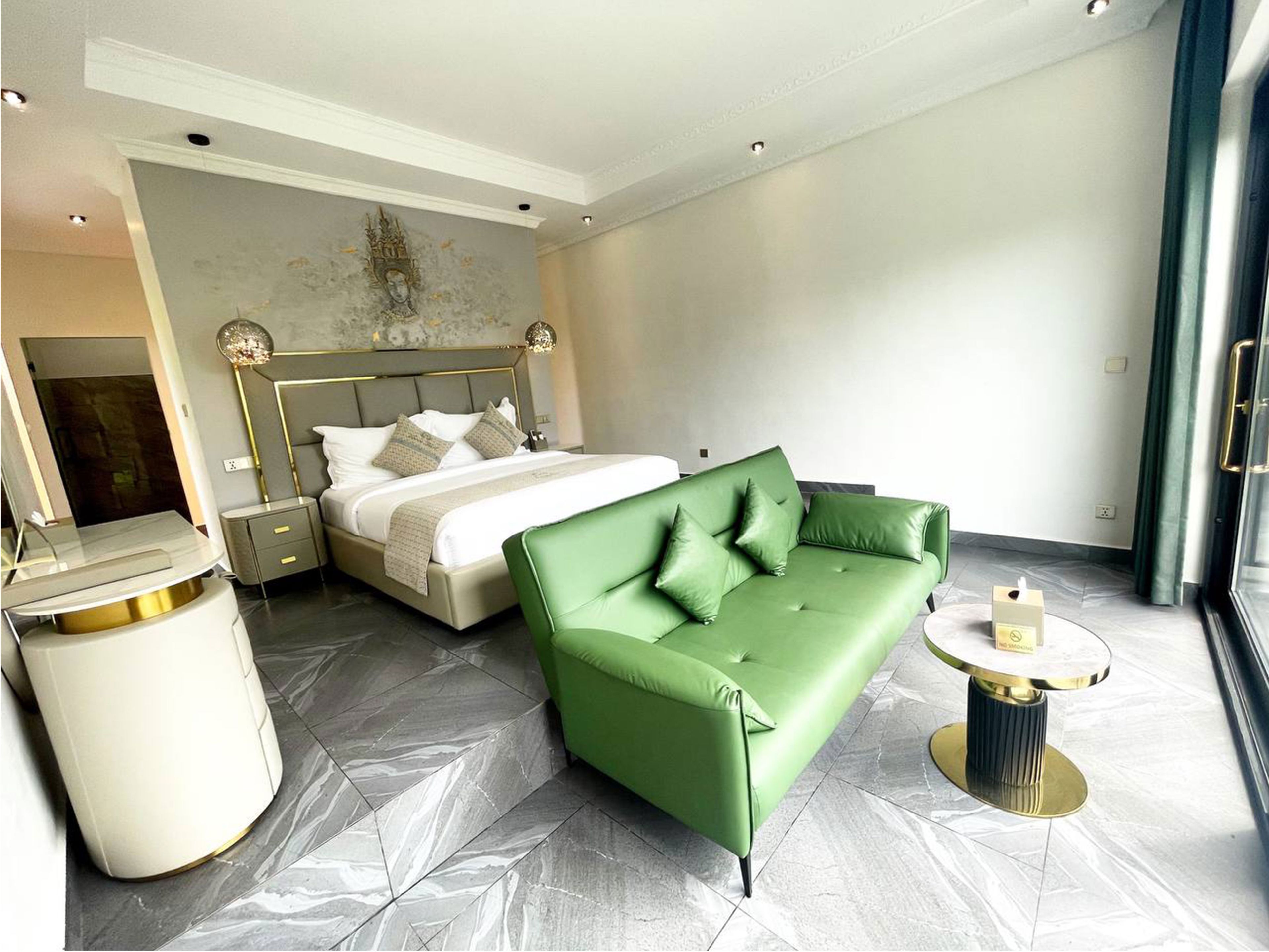 A modern hotel room with a bed, a green sofa, a small round table, and a trash bin.