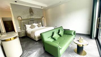 A modern hotel room with a bed, a green sofa, a small round table, and a trash bin.