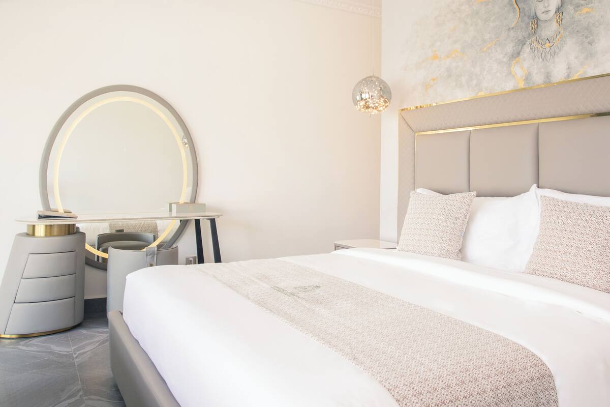 A modern bedroom with a large bed, a round mirror, and a decorative wall piece.