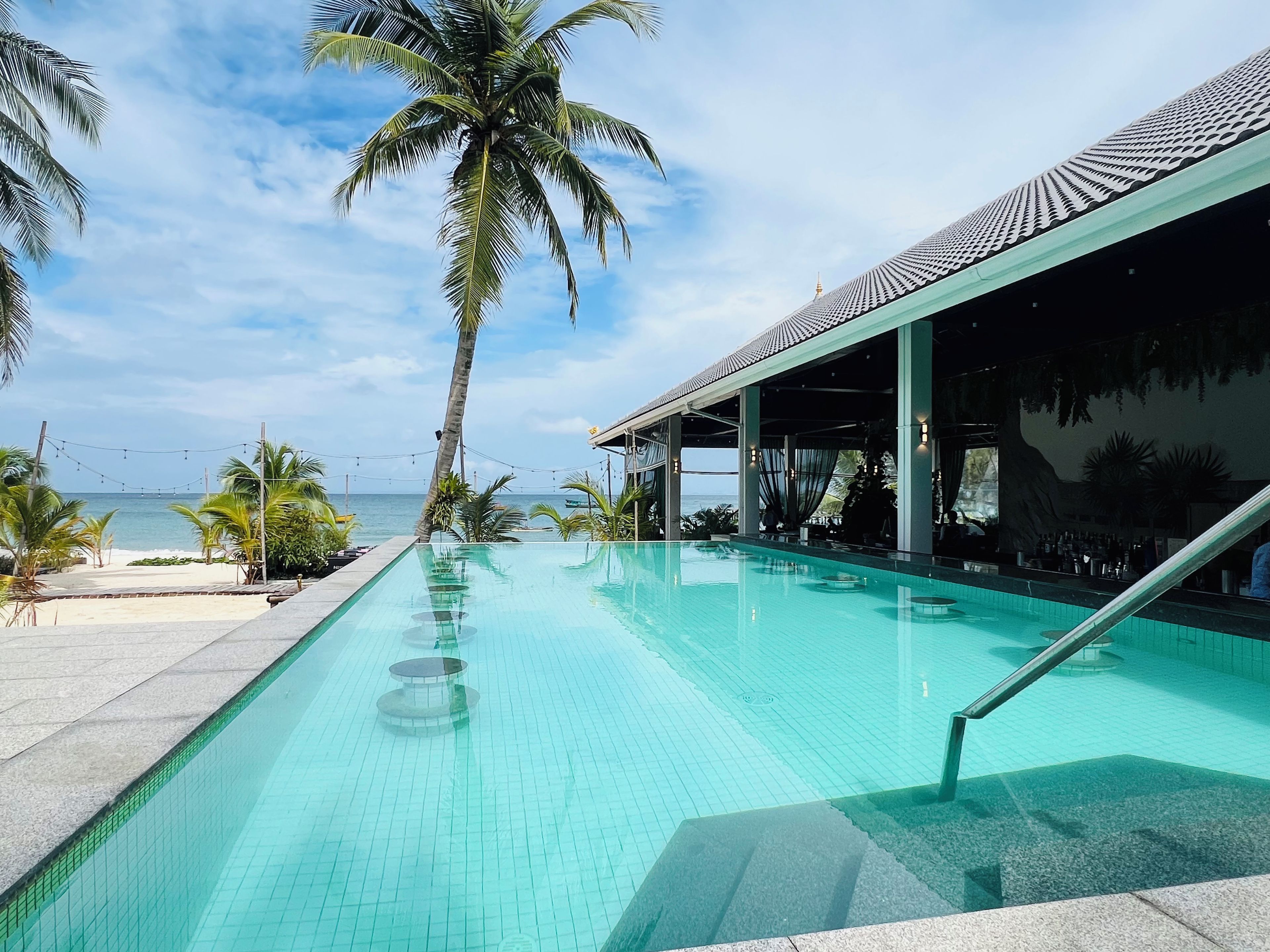 Una piscina con vista al mar, zona de bar y palmeras.