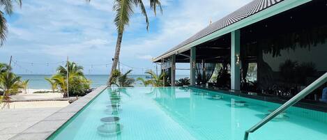 Una piscina con vista al mar, zona de bar y palmeras.