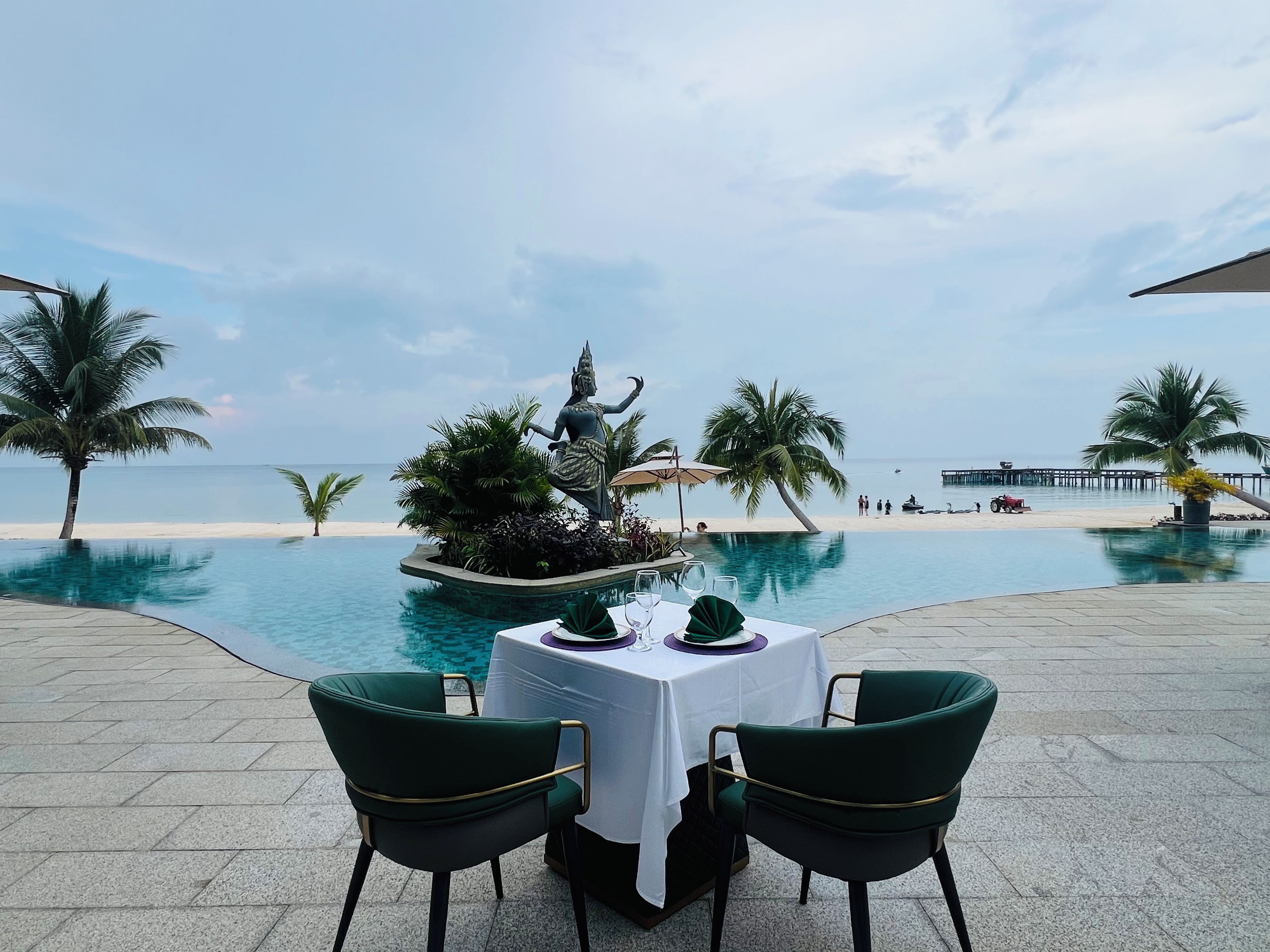 A dining area with a view of the ocean, a statue, and a pool.