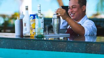 Un cantinero preparando una bebida en un bar junto a la piscina, con varias botellas y un shaker a la vista.