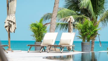 Zona junto a la piscina con sillones y sombrillas, palmeras y vista al océano.