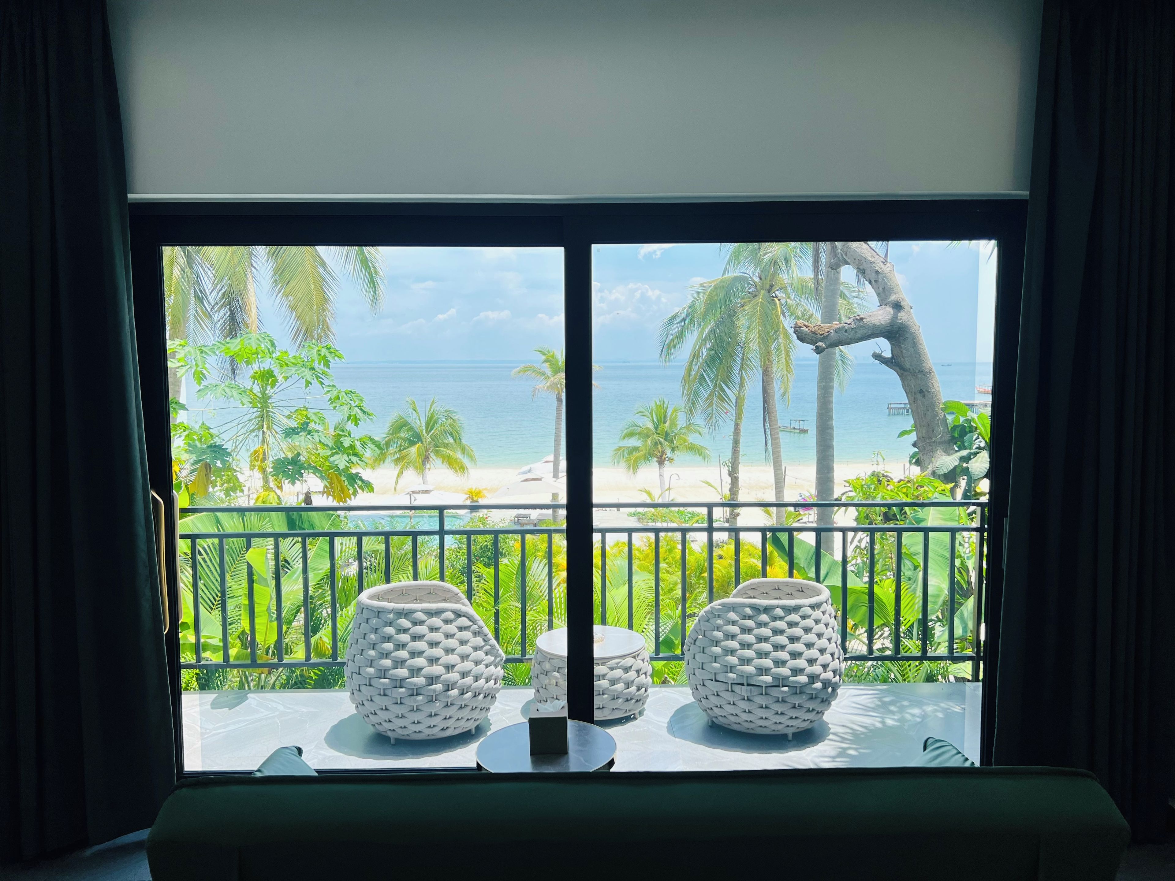 Quarto com vista para a praia, dois cachepots brancos trançados sobre uma mesa e um corrimão de varanda.