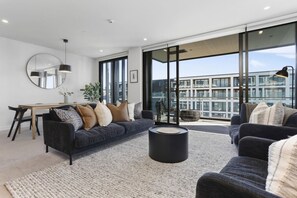 Un salon moderne avec un canapé foncé, une table basse ronde et un coin repas comprenant une table et des chaises en bois.