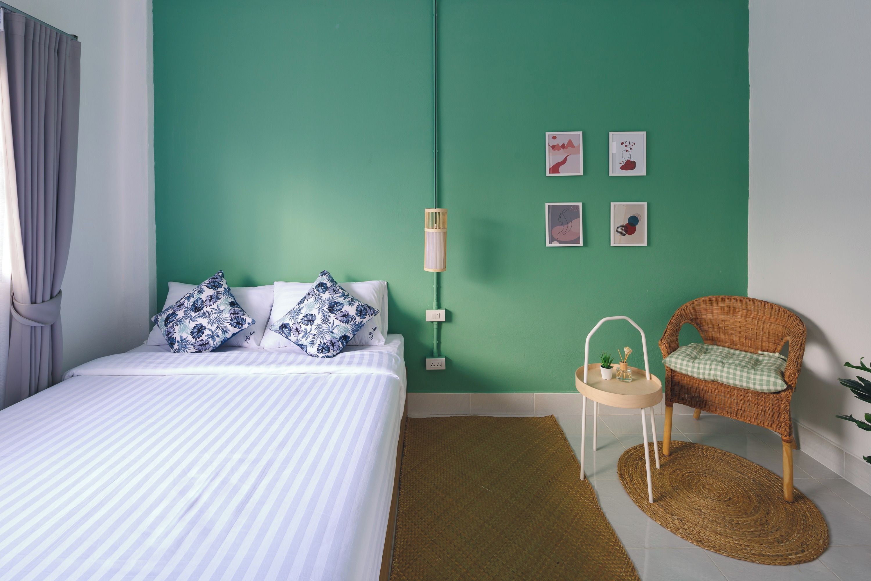 A bedroom with a bed, a wicker chair, a small table, and wall art.