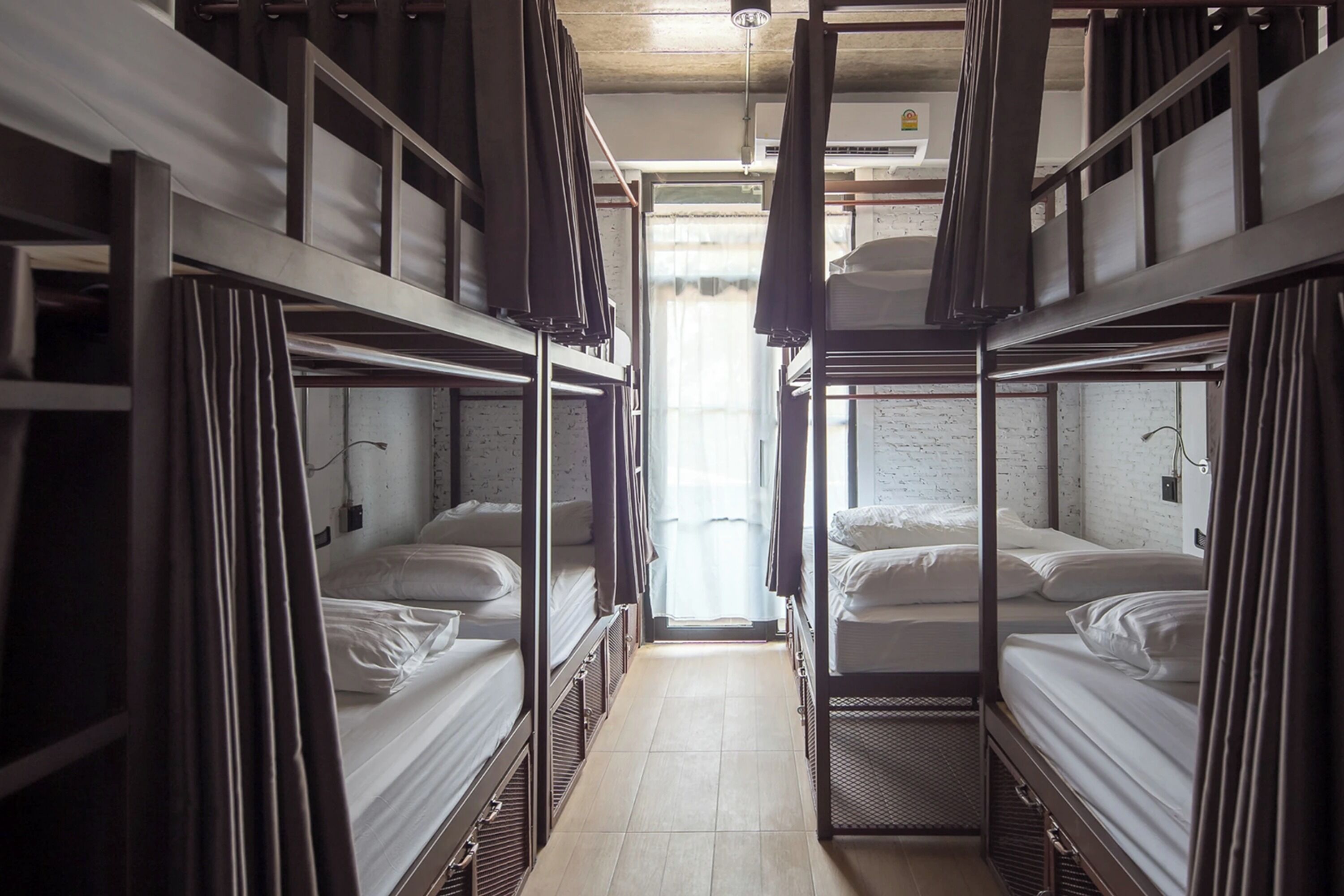 A corridor with bunk beds, a tiled floor, and a window with curtains.