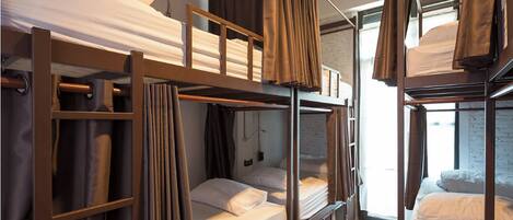 A bunk bed room with a window, curtains, and a visible electrical outlet.