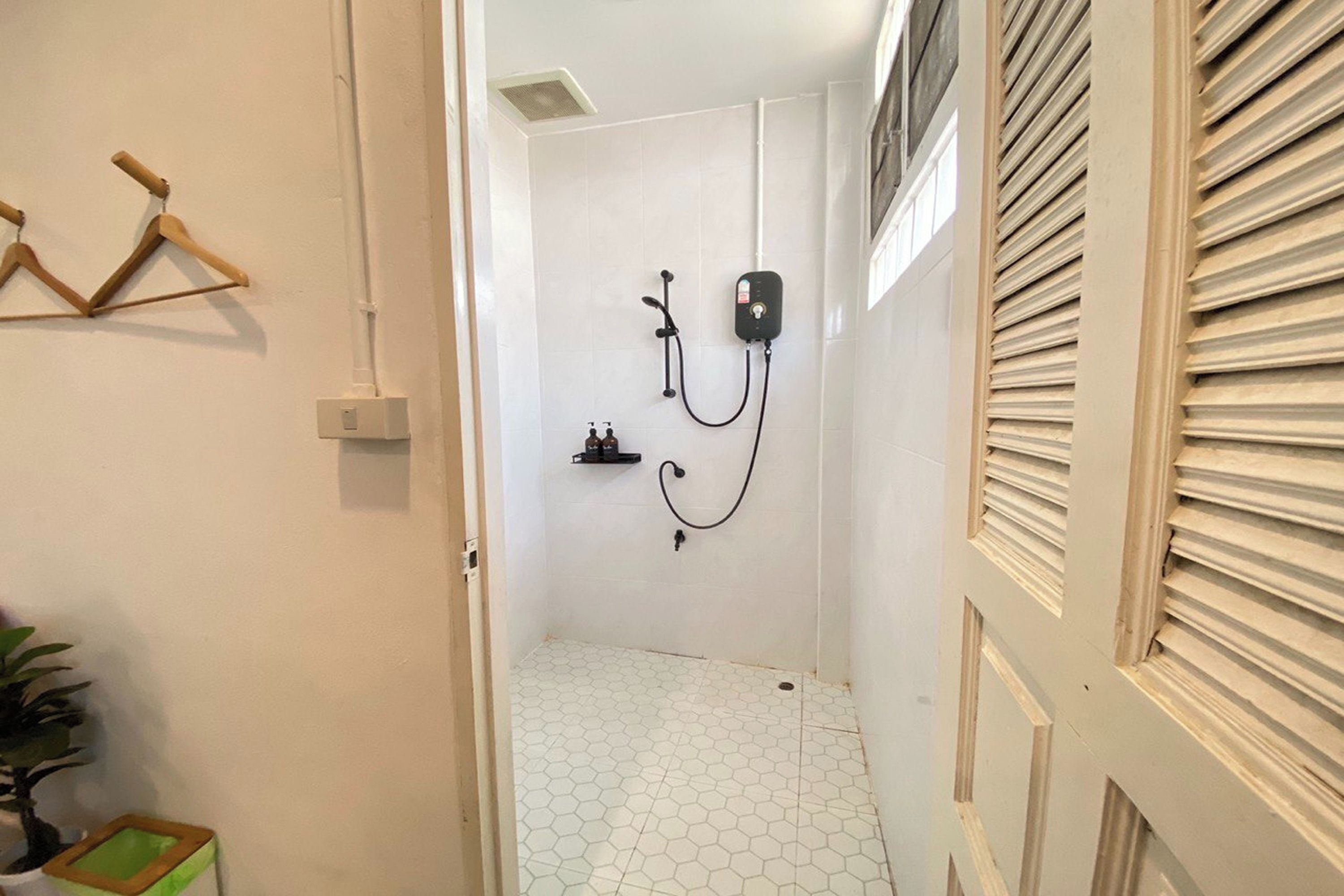 Corredor estreito que dá para um espaço com chuveiro, revestido por piso de azulejos hexagonais brancos, toalheiro e aquecedor na parede.