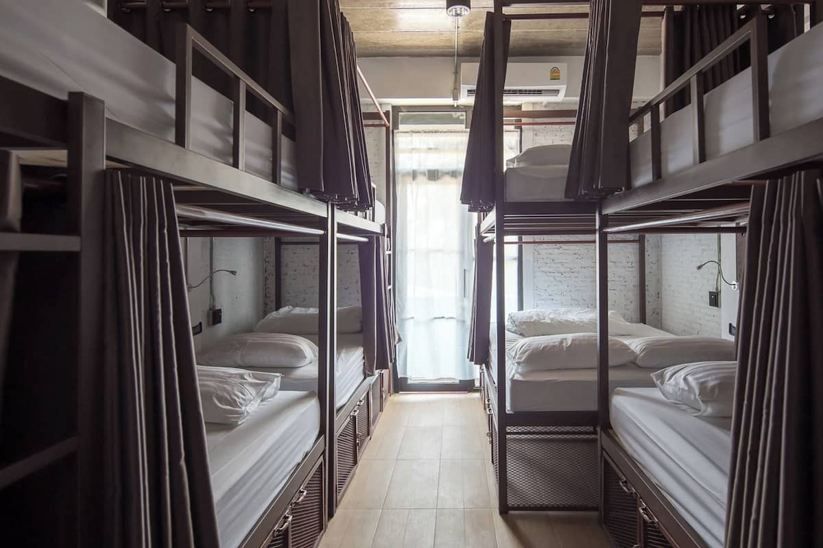 A corridor with bunk beds, each with a mattress and pillows, and a door at the end leading to a brighter area.