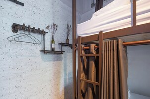 Una cama litera con cortina, un perchero metálico y un estante con una botella y plantas secas.
