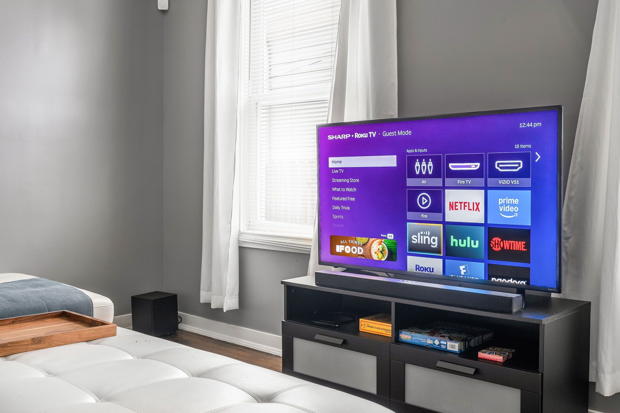 A modern living room with a flat-screen TV displaying a Roku interface, a white sofa, a wooden tray, and a black speaker.