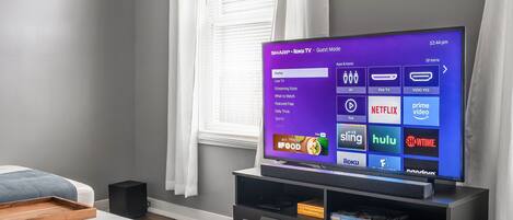 A modern living room with a flat-screen TV displaying a Roku interface, a white sofa, a wooden tray, and a black speaker.