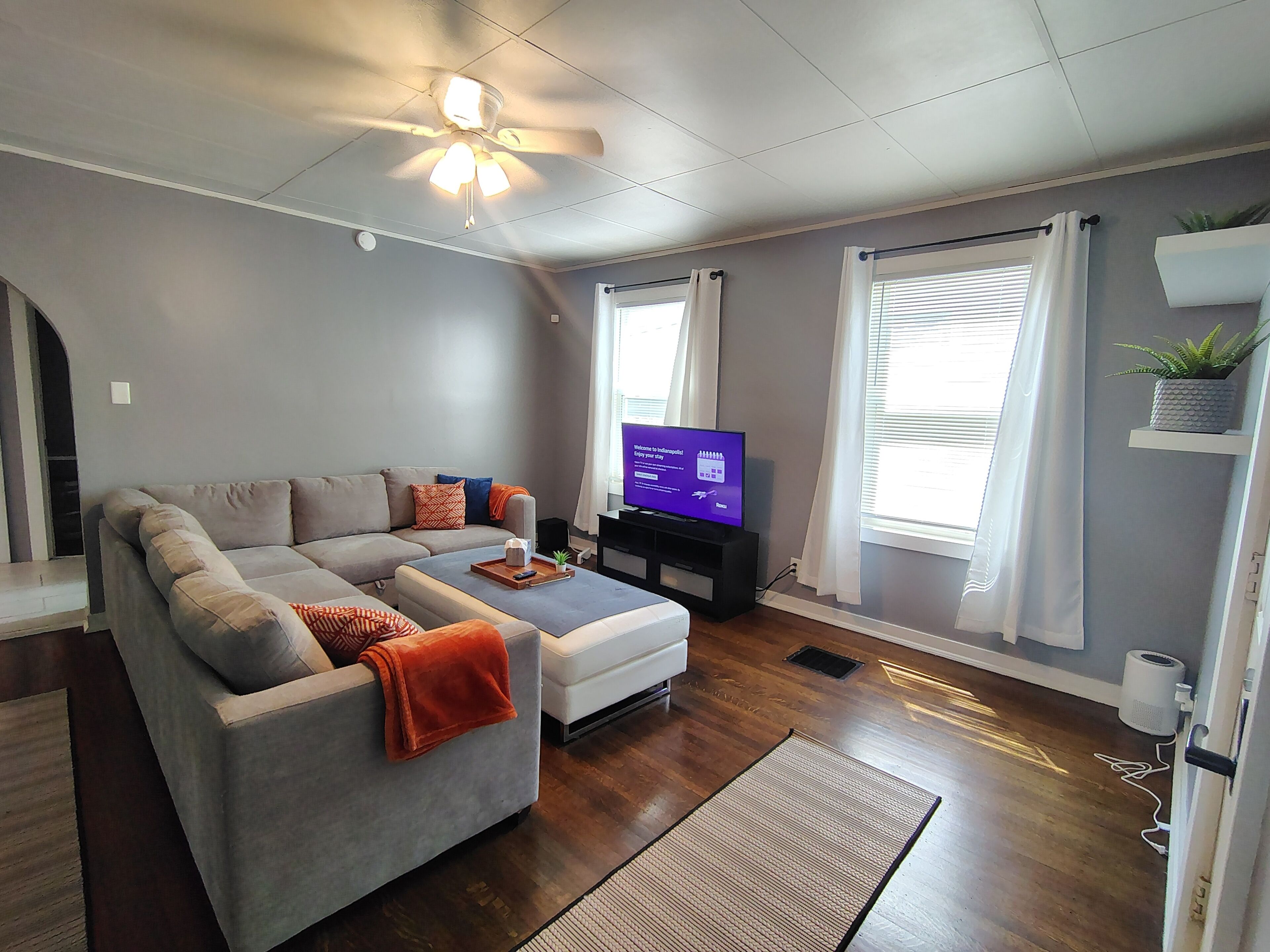 A living room with a sofa, a television, a ceiling fan, and a window with curtains.