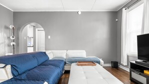 Una sala de estar moderna con un sofá seccional, un reposapiés blanco, un televisor de pantalla plana y una mesita de noche de madera.