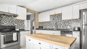 Una cocina moderna con armarios blancos, encimera de madera, electrodomésticos de acero inoxidable y un salpicadero con diseño.
