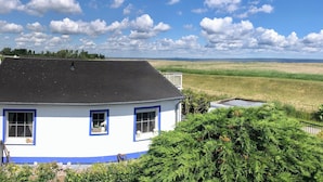 Un bâtiment blanc orné de bordures bleues et surmonté d’un toit noir, entouré de verdure et offrant une vue sur un paysage plat.