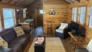 Interior acogedor de una cabaña con techo de madera, un sofá, televisor y comedor.