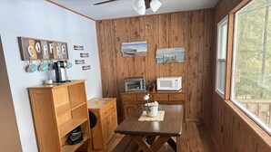 Cocina con paneles de madera, una mesa y un banco de madera, estación de café y vista a través de un ventanal grande.