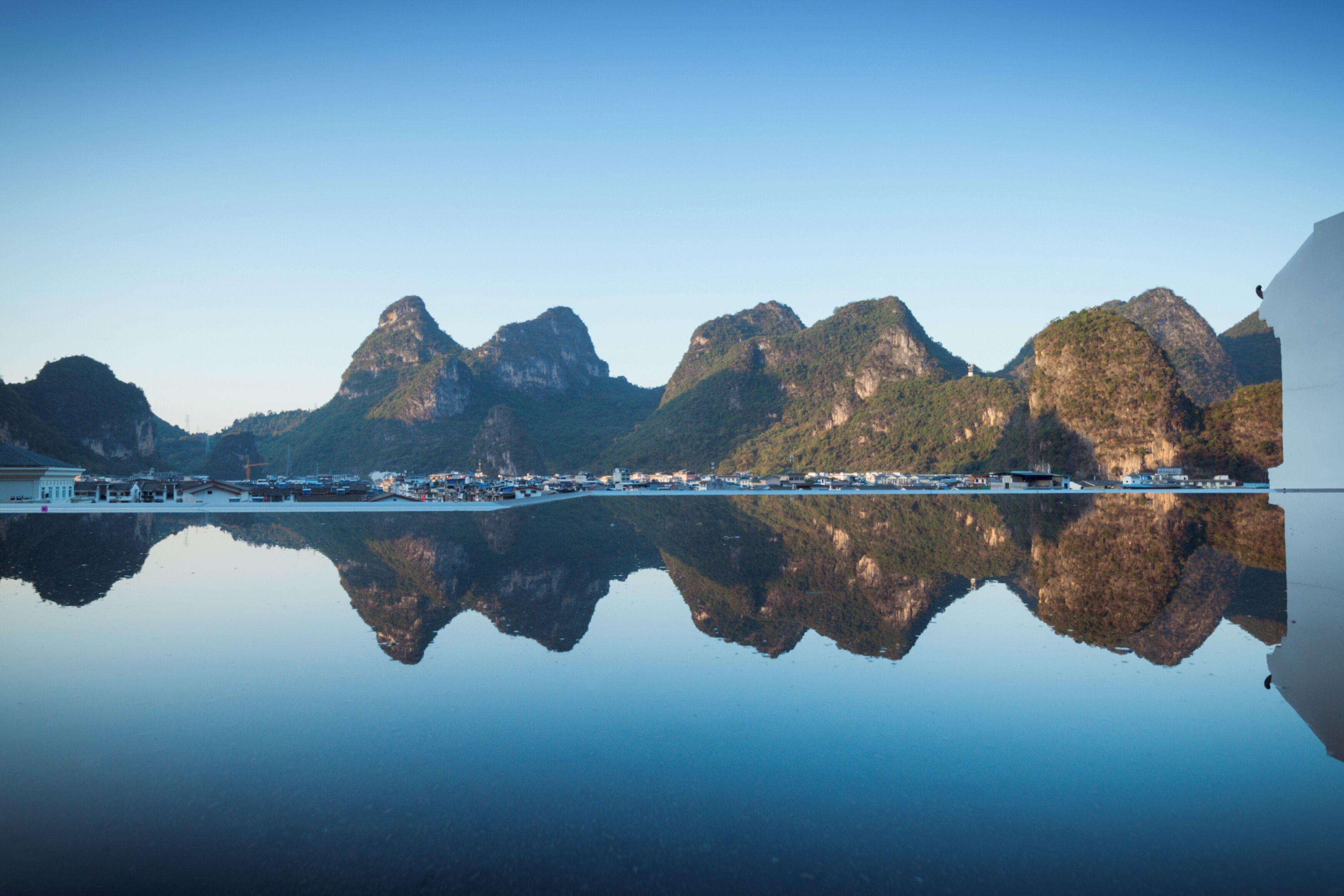 Ein ruhiger See spiegelt gebirgiges Gelände und eine kleine Stadt mit Häusern am Ufer.