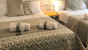 Hotelkamer met twee bedden, elk met beddengoed en kussens met een patroon, een nachtkastje met twee flessen en een hoofdbord met een lamp.