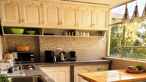 Een keuken met witte kastjes, een houten eettafel en een raam met uitzicht.