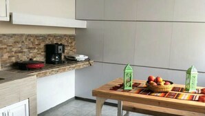Een moderne keuken met een houten tafel, een bank, een koffiezetapparaat en een mand met fruit.