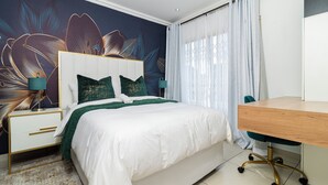 A bedroom with a bed, a desk, and a nightstand.