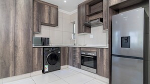 A modern kitchen with wooden cabinets, a stainless steel refrigerator, a washing machine, and an oven.