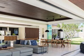 Un salon moderne avec un canapé, une table à manger et des chaises, une cuisine en arrière-plan et une vue sur un jardin.