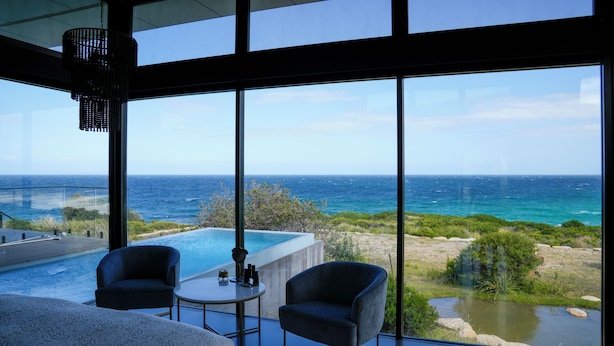 Une chambre moderne dotée d’une grande fenêtre donnant sur l’océan, d’une petite piscine et de deux fauteuils.