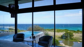 Una habitación moderna con un amplio ventanal con vistas al océano, una pequeña piscina y dos sillas.