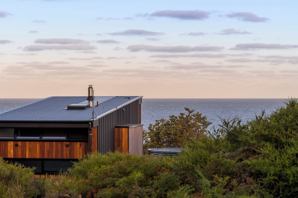 A modern coastal house with a flat roof, large windows, and a chimney.