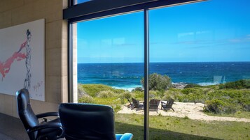 Una habitación con un amplio ventanal con vistas al océano, un cuadro en la pared y dos sillas.