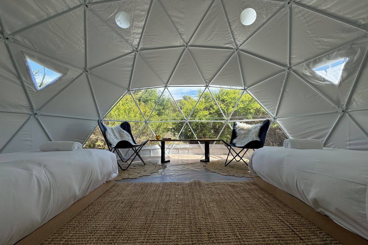A dome-shaped tent with two beds, a small table, and two chairs.
